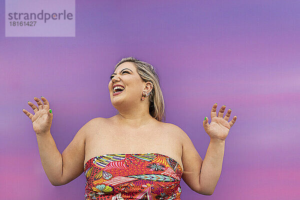 Fröhliche junge Frau gestikuliert vor einer lila Wand