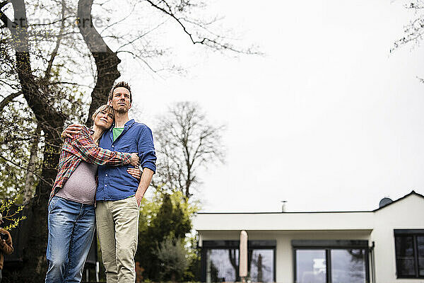 Reifer Mann umarmt schwangere Frau vor dem Haus