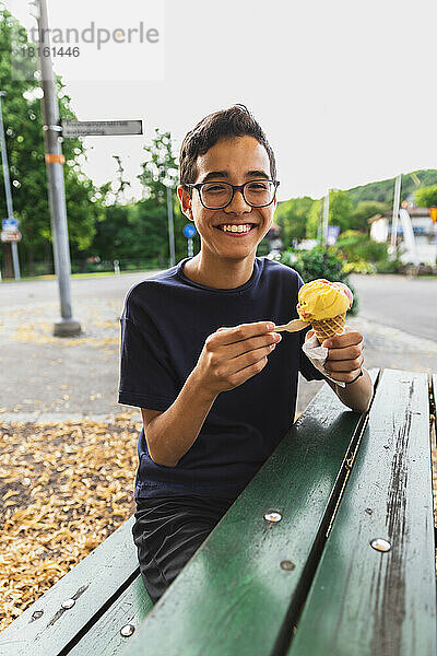 Happy boy enjoying ice cream sitting on bench