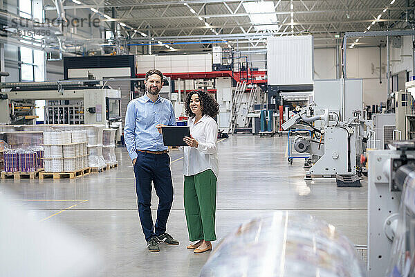 Lächelnde Geschäftsfrau mit Tablet-PC steht dem Geschäftsmann in der Fabrik zur Seite