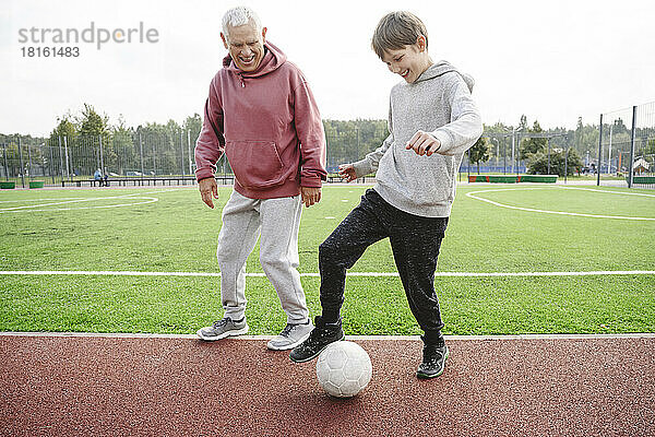 Glücklicher Junge mit Großvater  der auf dem Sportplatz mit Fußball spielt