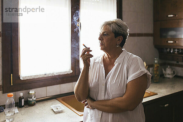 Depressive Frau raucht zu Hause in der Küche Zigarette