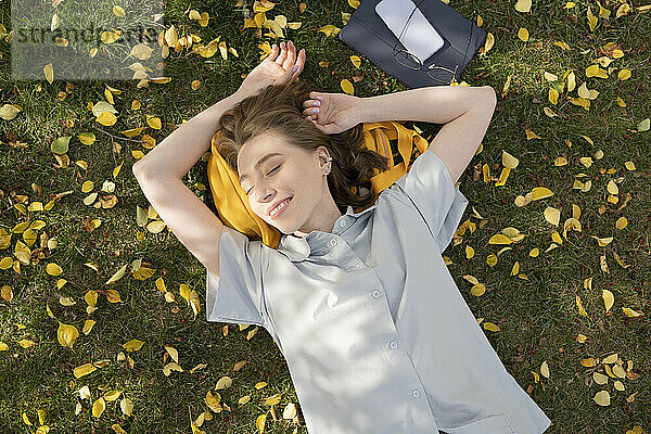 Lächelnde junge Frau mit geschlossenen Augen liegt im Herbstpark