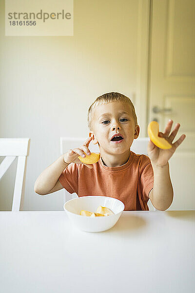 Junge hält Apfelscheiben am Esstisch zu Hause
