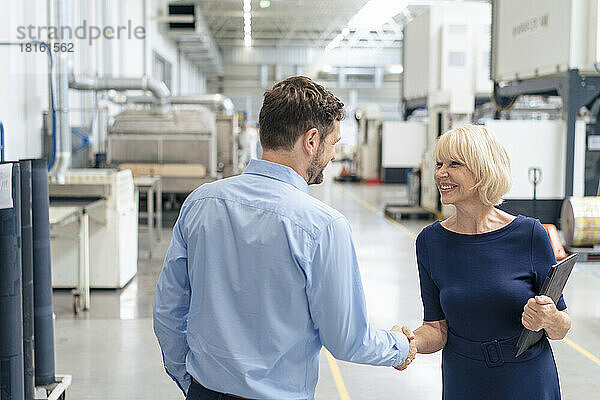 Smiling senior businesswoman holding laptop shaking hand with businessman