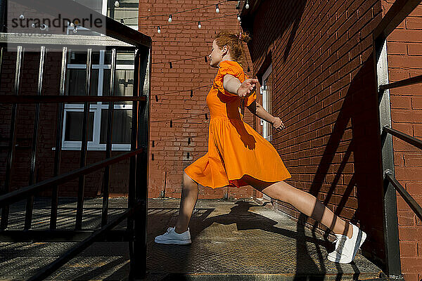 Frau im orangefarbenen Kleid wärmt sich an einem sonnigen Tag auf