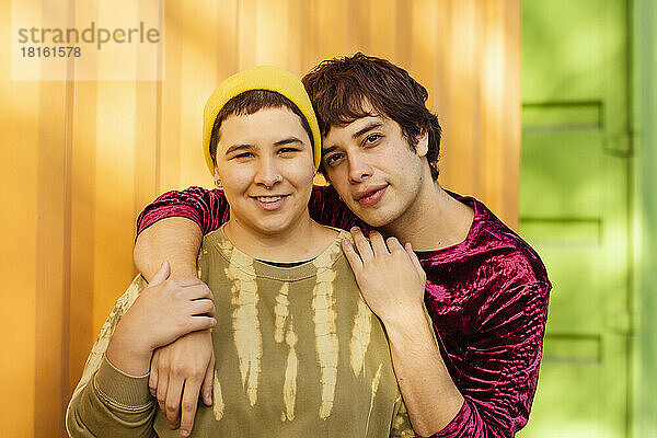 Lächelndes nicht-binäres Paar  das vor einem gelben Frachtcontainer steht