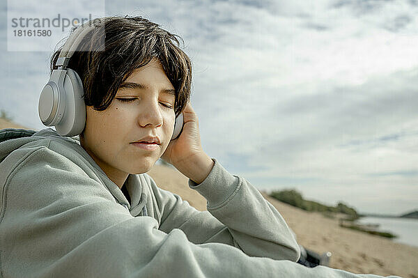 Junge mit geschlossenen Augen hört am Strand Musik über kabellose Kopfhörer