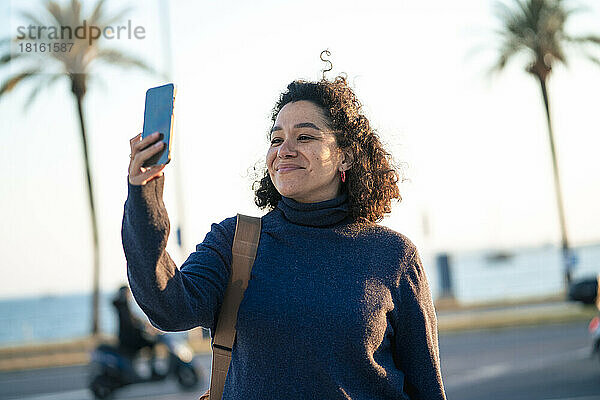 Lächelnde Geschäftsfrau  die an einem sonnigen Tag ein Selfie mit dem Smartphone macht