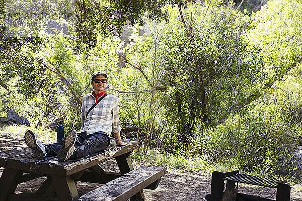 Glücklicher Mann mit Sonnenbrille auf Holztisch im Wald