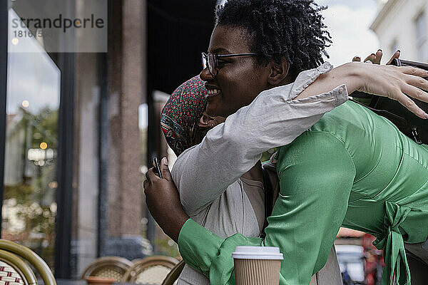 Glückliche Frau umarmt Freundin im Straßencafé