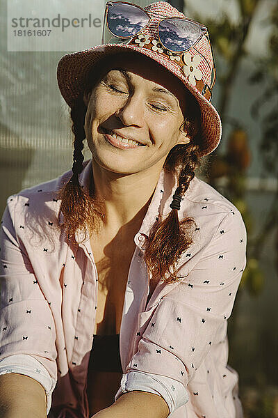 Lächelnde Frau mit Hut sitzt mit geschlossenen Augen