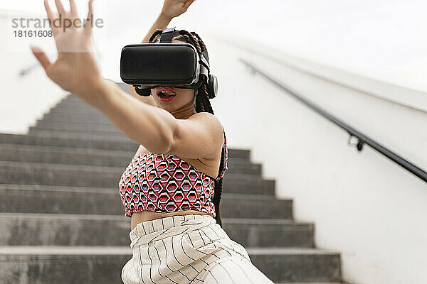 Junge Frau mit Virtual-Reality-Simulator gestikuliert auf der Treppe