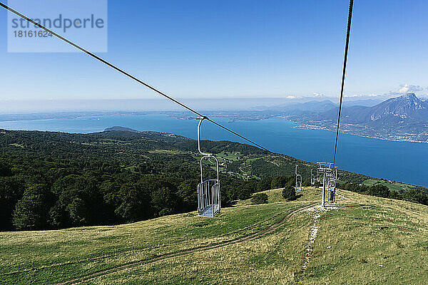 Elevated view of chair lifts hanging from cables over green mountain near Lake Garda