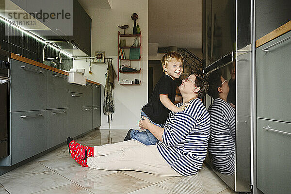 Glücklicher Sohn und Mutter sitzen auf dem Boden in der Küche
