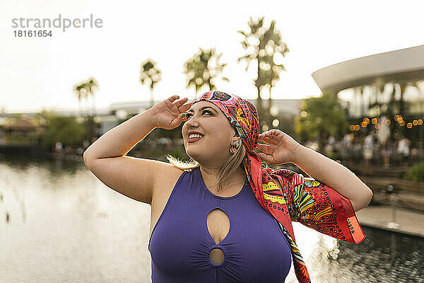 Glückliche junge Frau mit buntem Kopftuch vor dem See