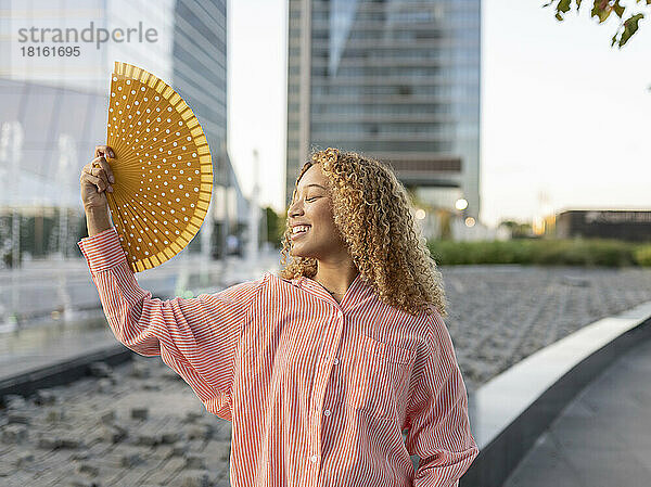 Lächelnde Frau mit geschlossenen Augen mit Faltfächer auf der Straße