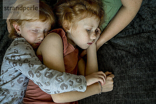 Liebevolle Geschwister umarmen sich und schlafen auf dem Schoß der Mutter