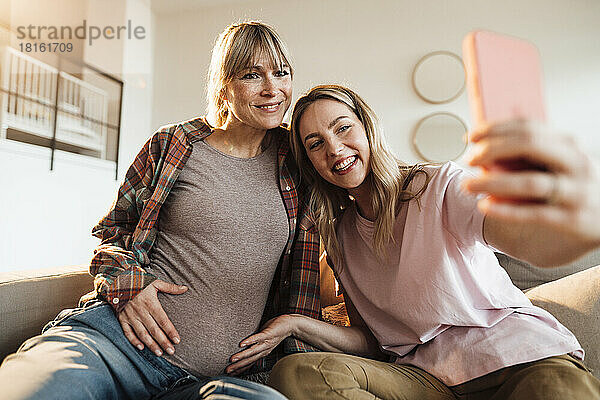 Glückliche Frau  die zu Hause ein Selfie mit ihrer werdenden Schwester per Smartphone macht