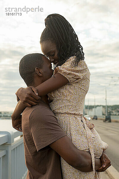 Junger Mann hebt seine Freundin hoch und umarmt sie an der Brücke