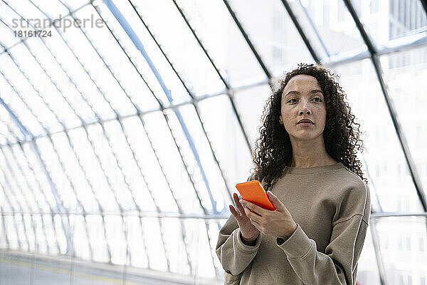 Nachdenkliche Frau steht mit Mobiltelefon am Bahnhof
