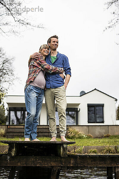 Glückliches werdendes Paar  das sich umarmt und auf dem Steg vor dem Haus steht