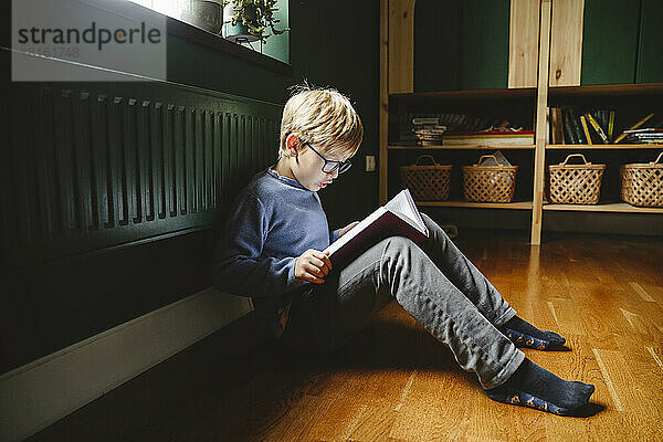 Junge liest ein Buch  das zu Hause auf dem Boden sitzt