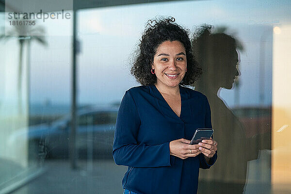 Glückliche Geschäftsfrau mit Smartphone vor Glas