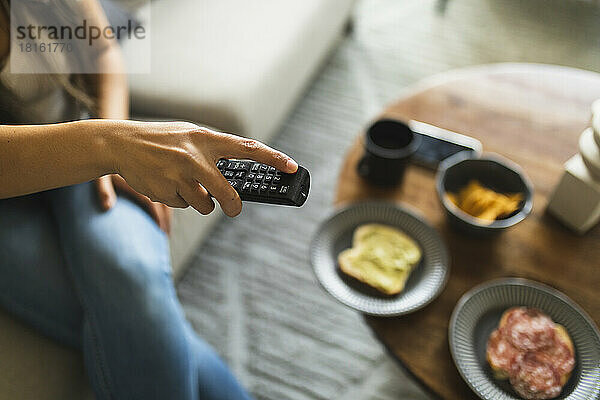 Young woman with TV remote control sitting at home