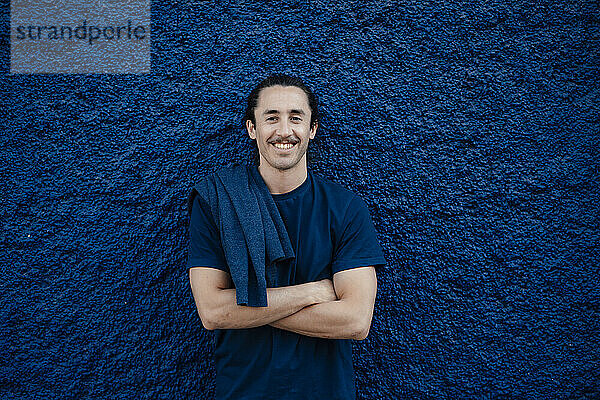Smiling young man with t-shirt in front of blue textured wall
