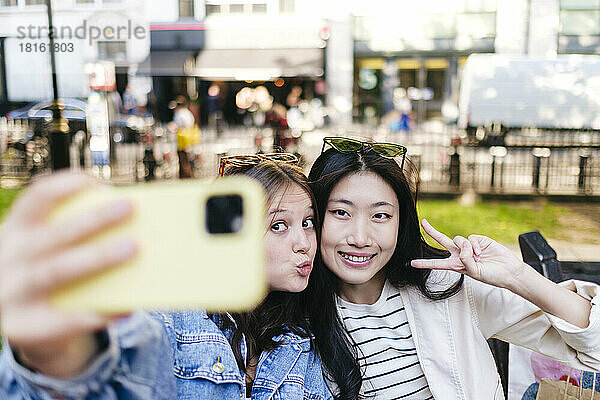 Woman showing peace sign taking selfie with lesbian friend through smart phone