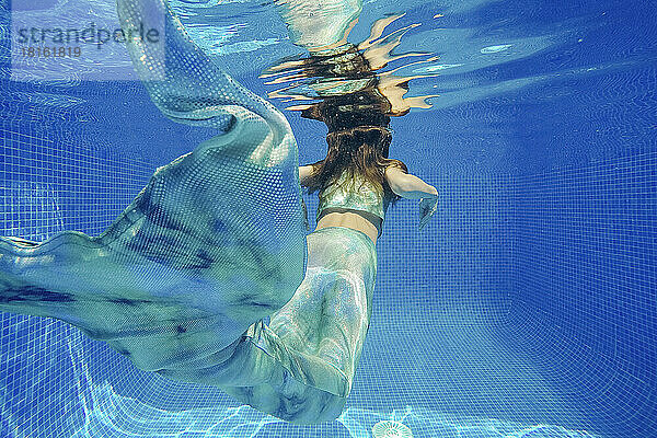 Mädchen im Meerjungfrauenkostüm schwimmt unter Wasser