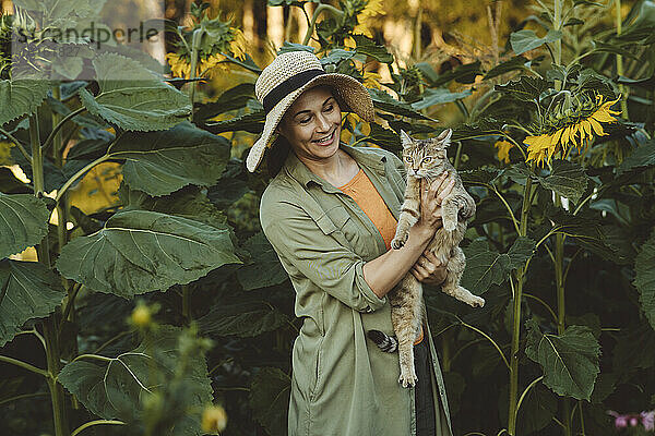 Lächelnde reife Frau hält getigerte Katze im Garten