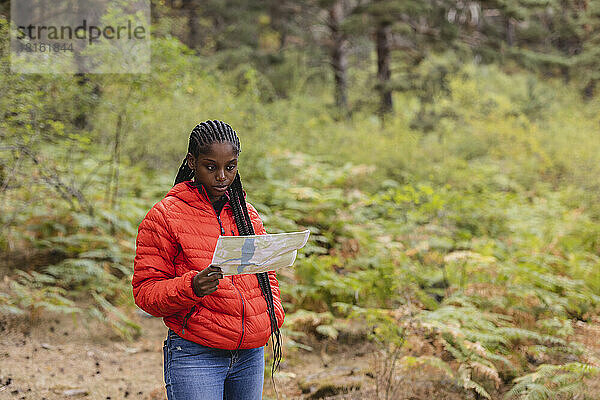 Junge Frau mit geflochtenen Haaren liest Karte im Wald