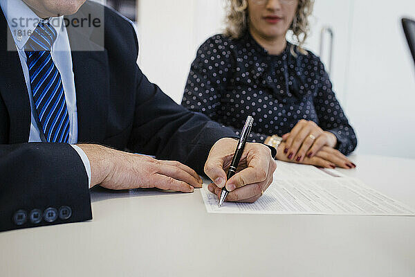 Reifer Geschäftsmann unterschreibt Dokument am Schreibtisch