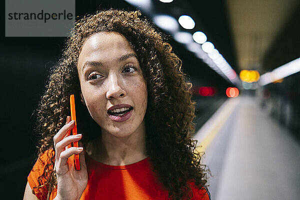 Junge Frau spricht am U-Bahnsteig per Smartphone