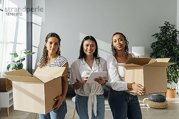 Lächelnde Frau mit Tablet-PC inmitten von Freunden  die Kisten im neuen Zuhause tragen