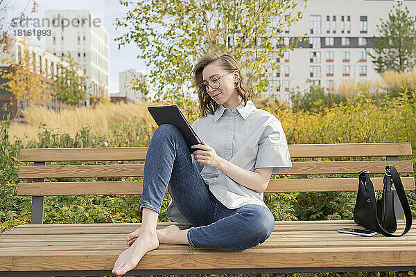 Junge Frau sitzt mit Tablet-PC auf Bank im Park