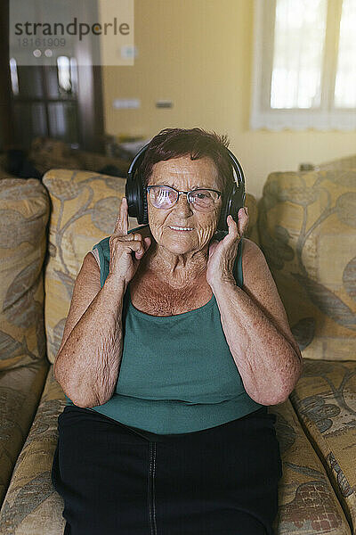 Glückliche ältere Frau  die zu Hause Musik über Kopfhörer genießt