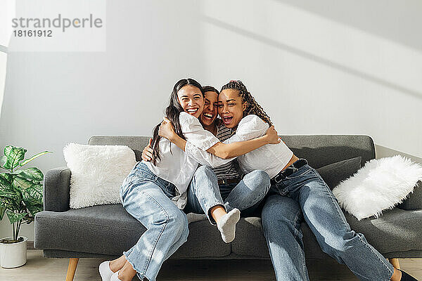 Happy friends embracing each other sitting on couch in living room