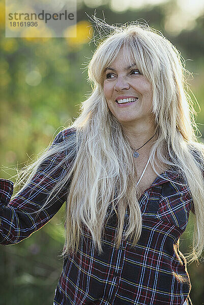 Glückliche blonde Frau mit langen Haaren an einem sonnigen Tag