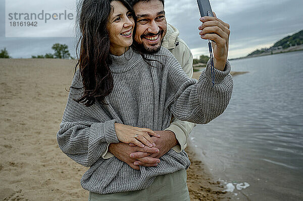 Frau mit Freund macht Selfie per Smartphone am Flussufer