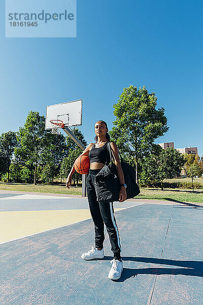 Selbstbewusste Sportlerin mit Basketball auf dem Sportplatz an einem sonnigen Tag