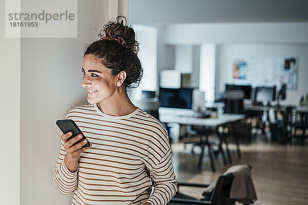 Lächelnde Geschäftsfrau mit Mobiltelefon im Büro