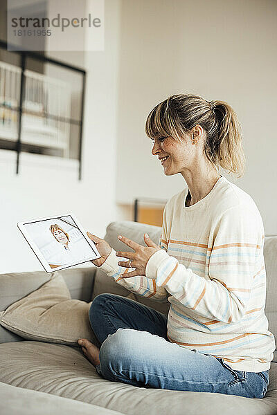 Schwangere Frau macht Online-Konsultation mit Arzt über Tablet-PC auf Sofa sitzend