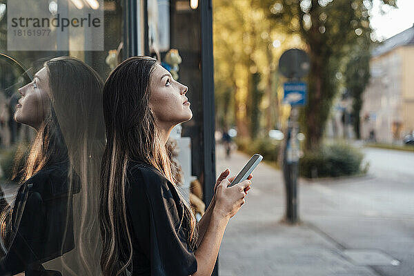 Junge Frau mit Mobiltelefon steht an Glaswand