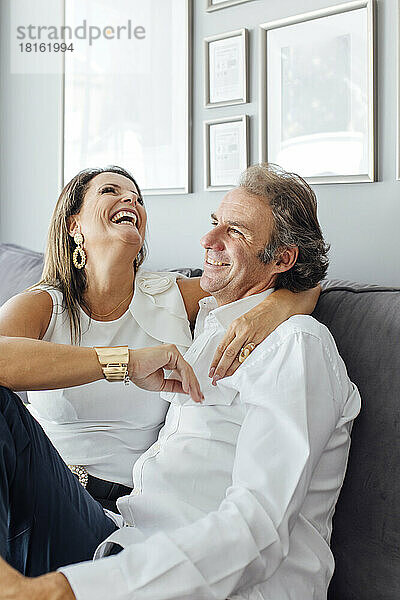 Woman with arm around man laughing on sofa in living room at home