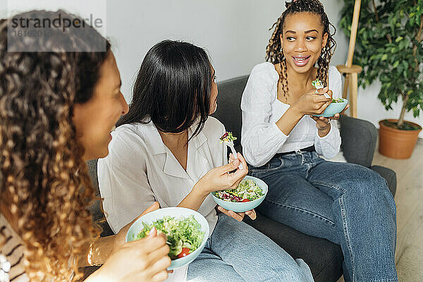Lächelnde Frau isst Salat mit Freunden im Wohnzimmer