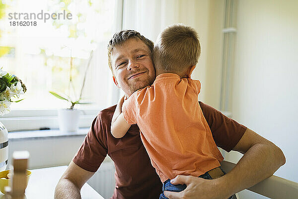 Junge umarmt lächelnden Vater zu Hause