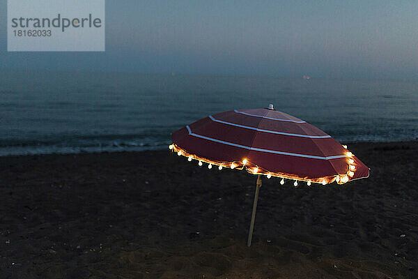 Beleuchtete Lichterkette auf rosa Sonnenschirm am Strand